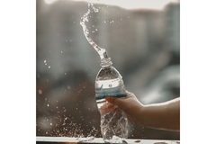 Image A hand squeezing a water bottle so water is sprouting out of the top.